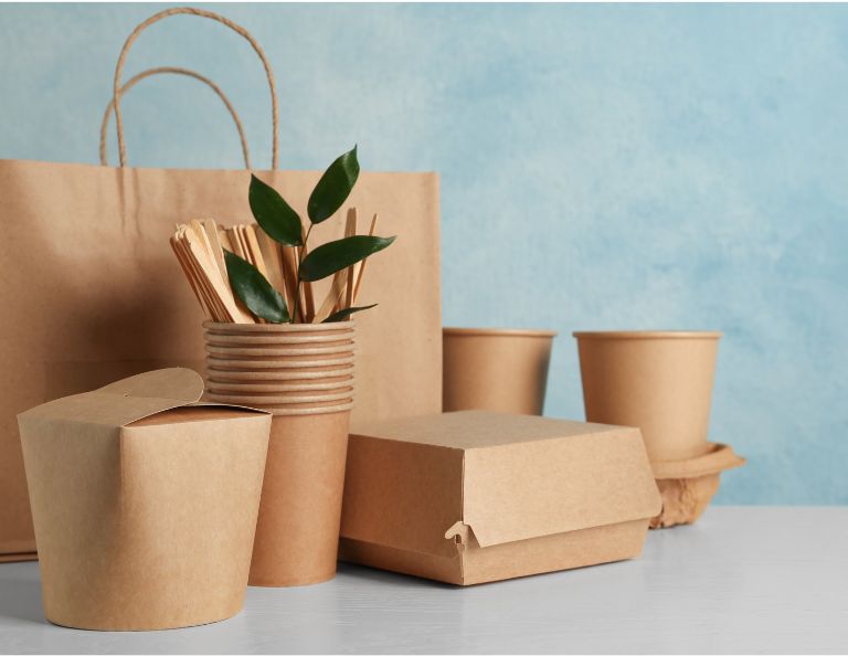 Eco-friendly and biodegradable food packaging, including cups, straws, and boxes, on a table.