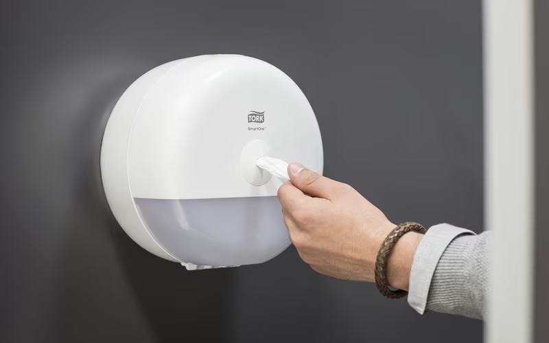 Hand using a Tork SmartOne toilet tissue dispenser, demonstrating Bay West Caribbean's high-quality hygiene and dispensing solutions.