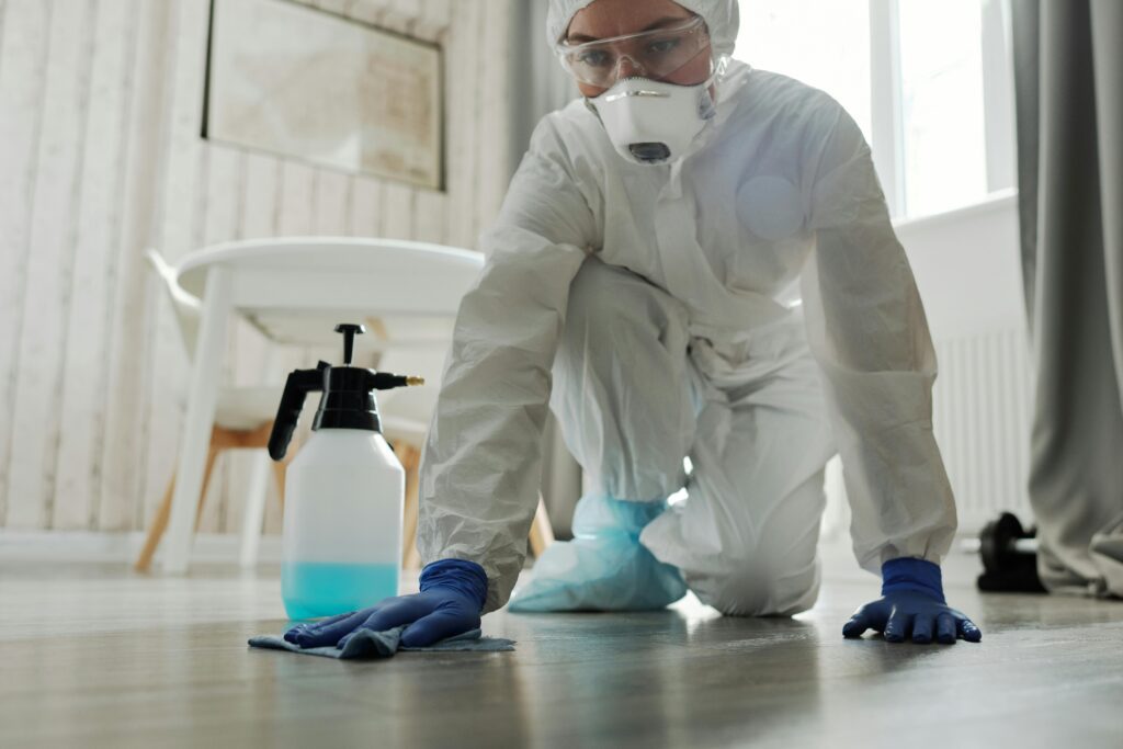 Professional cleaner wearing protective gear sanitizing a floor with cleaning spray.