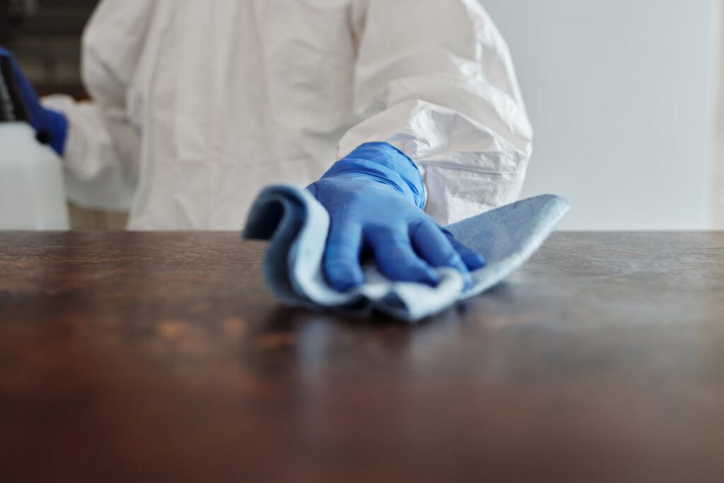 protective gear cleaning a surface with blue gloves and a cloth.