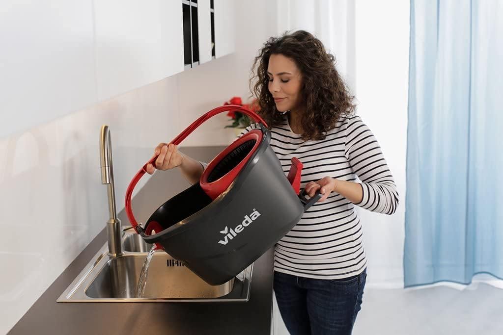 Smiling woman using a Vileda mop bucket in a modern kitchen, showcasing Bay West Caribbean's professional cleaning tools.